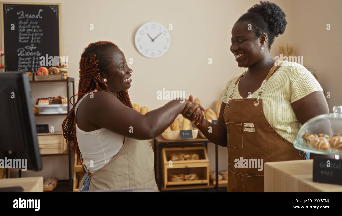 African american women bakers working together indoors at a cozy bakery shop, smiling and shaking hands. Stock Photo