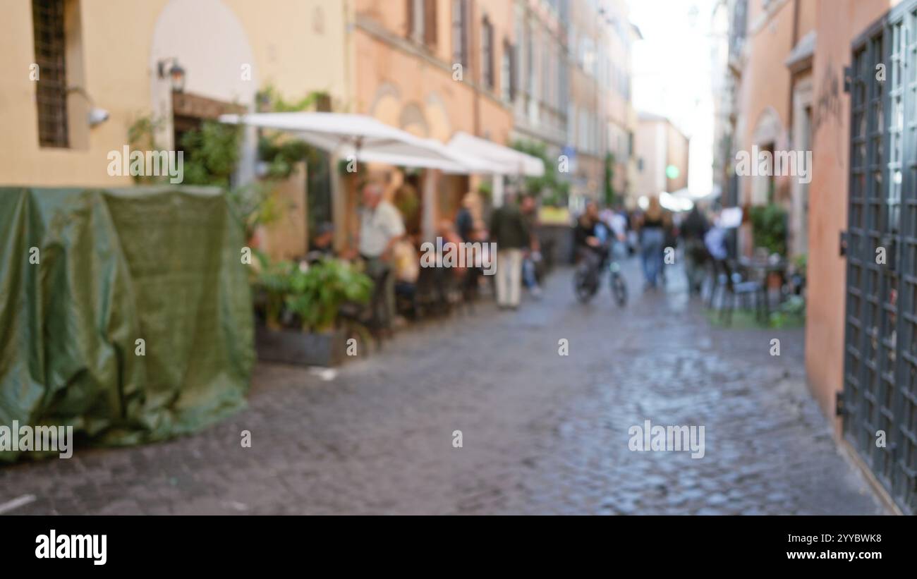 Blurred image of people walking and dining outdoors on a cobblestone ...