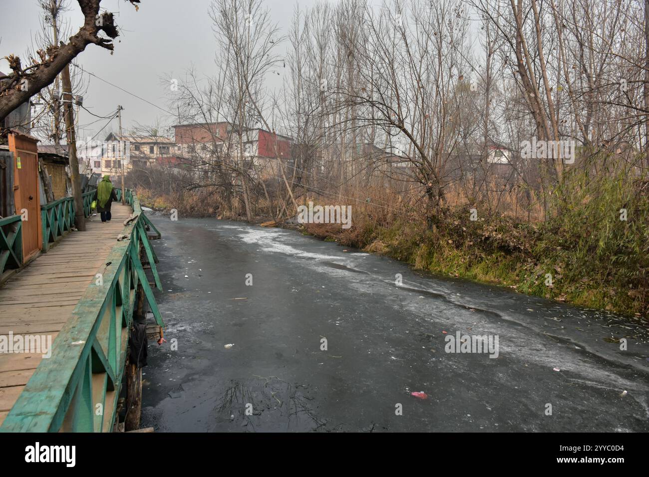 a-woman-walks-along-the-wooden-foot-bridge-as-a-dal-lake-is-seen