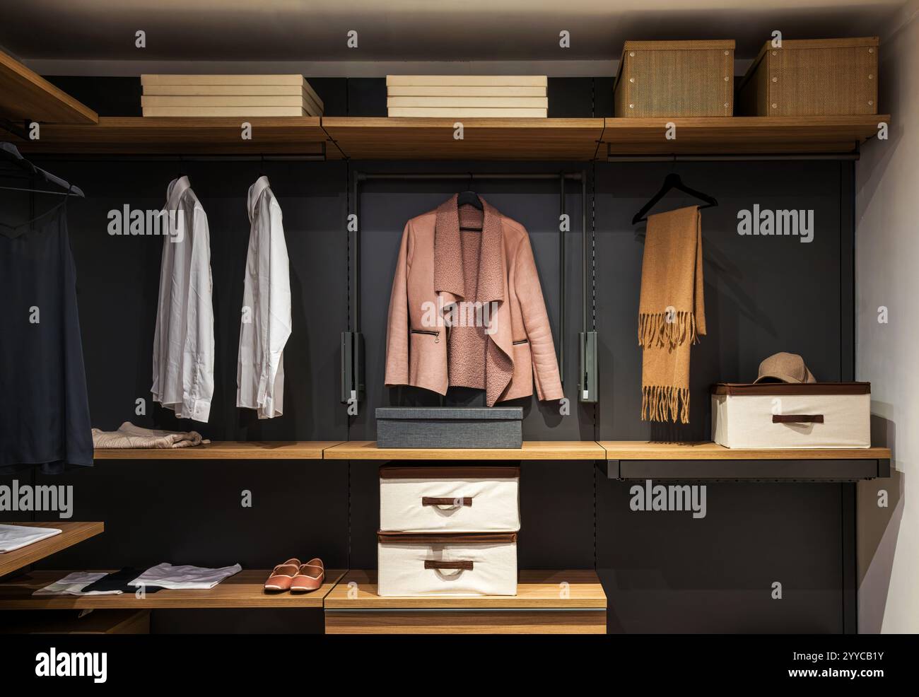 Contemporary walk in closet showcasing neatly arranged clothing, shoes, and accessories on wooden shelves and hanging racks Stock Photo