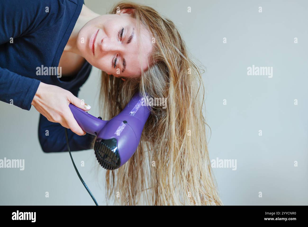 Young woman drying her hair with a hairdryer isolated on studio ...