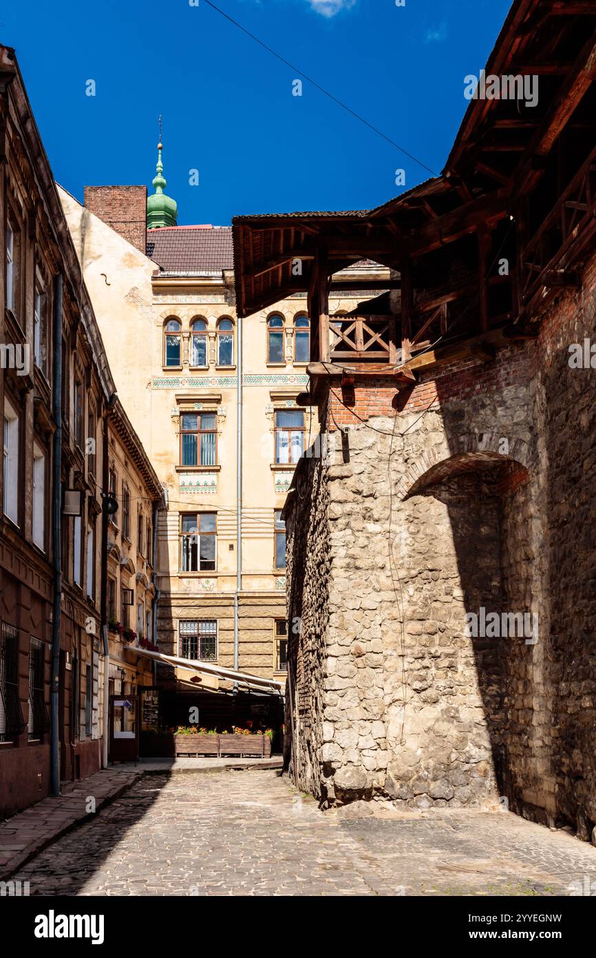 A narrow alleyway with a building in the background. The building has a green roof. The alleyway is empty and the sun is shining brightly Stock Photo