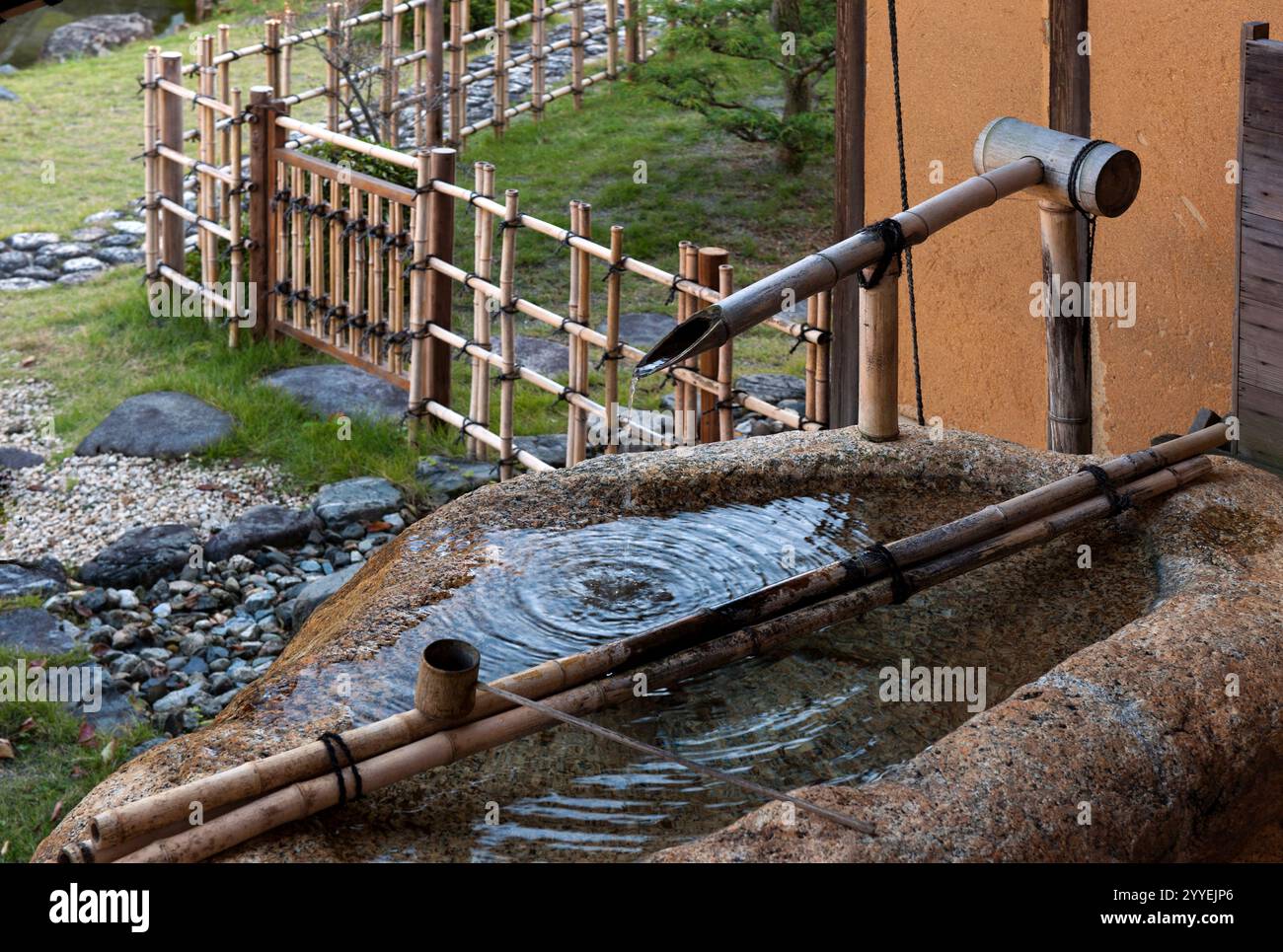 Water drips gently from a bamboo spout into a 'tsukubai' (stone basin) as a garden element feature in a Japanese contemplation garden in Hikone, Japan Stock Photo