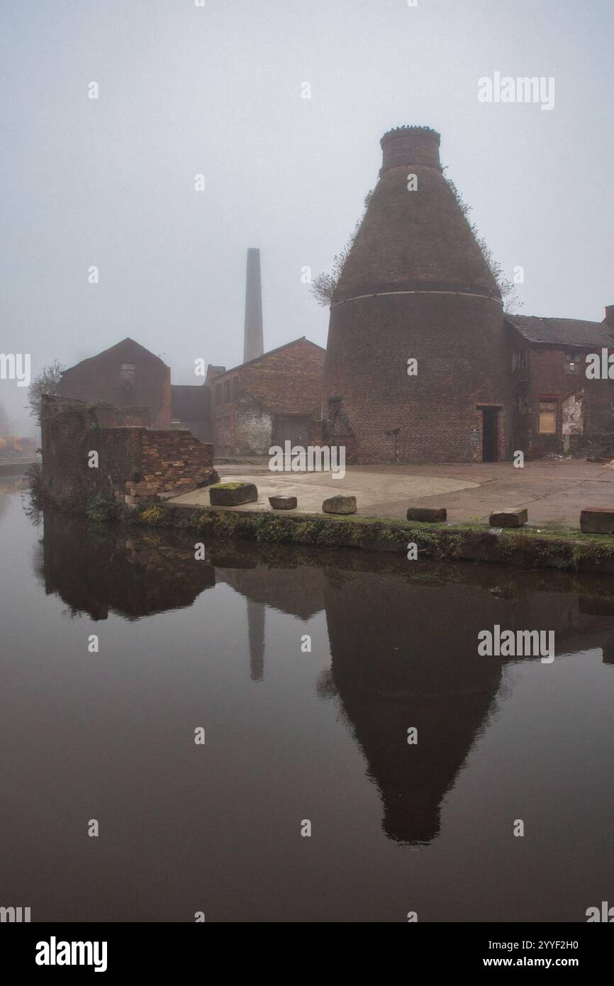 An old bottle kiln in Stoke on Trent is reflected in the canal. Taken on a foggy day to create an atmosphere it is reflected in the canal Stock Photo