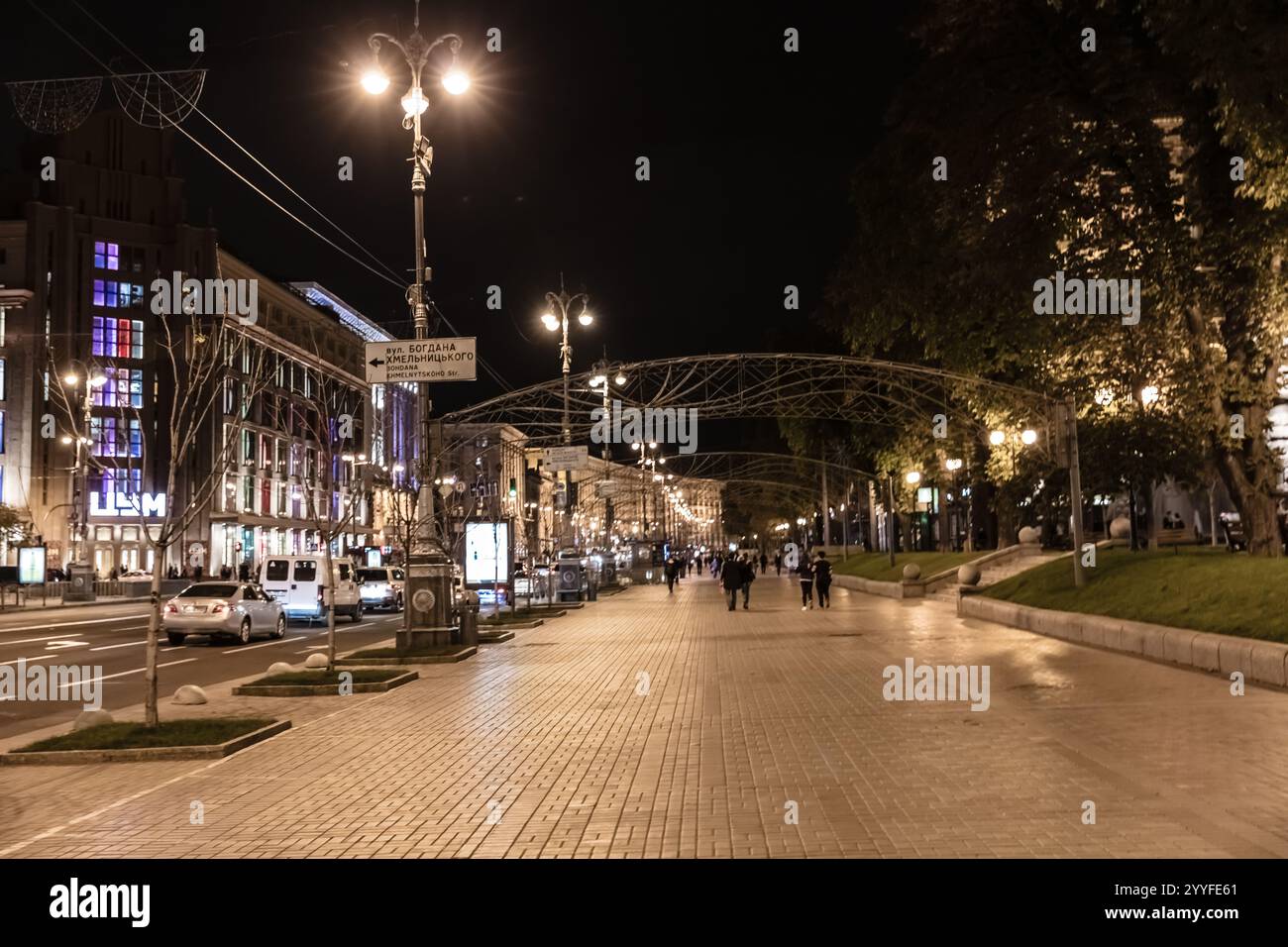 A city street at night with people walking and cars driving. The street ...