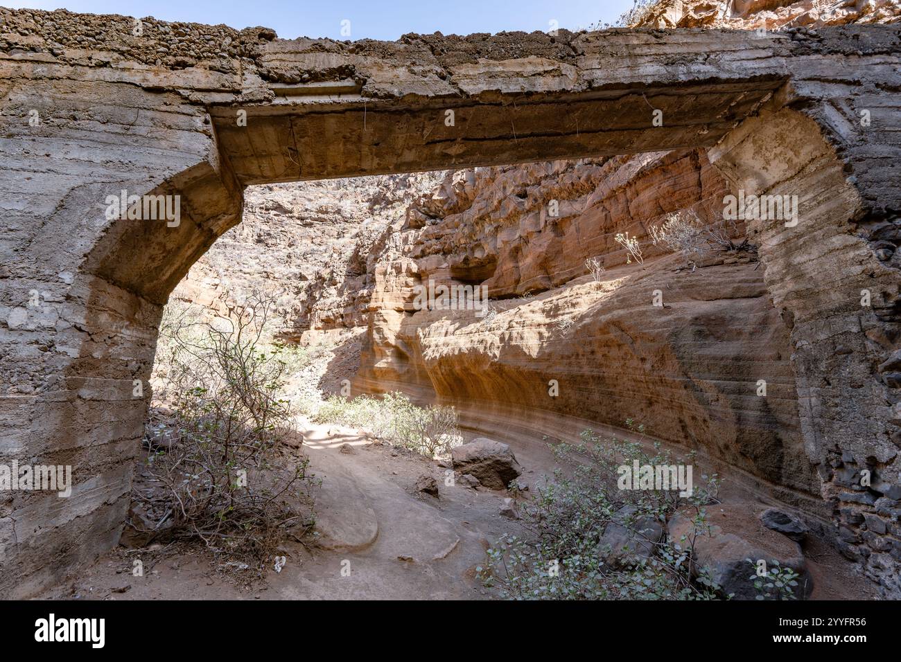 A bridge made of stone is seen through a small opening. The bridge is arched and the sunlight is shining through it. The scene is peaceful and serene Stock Photo