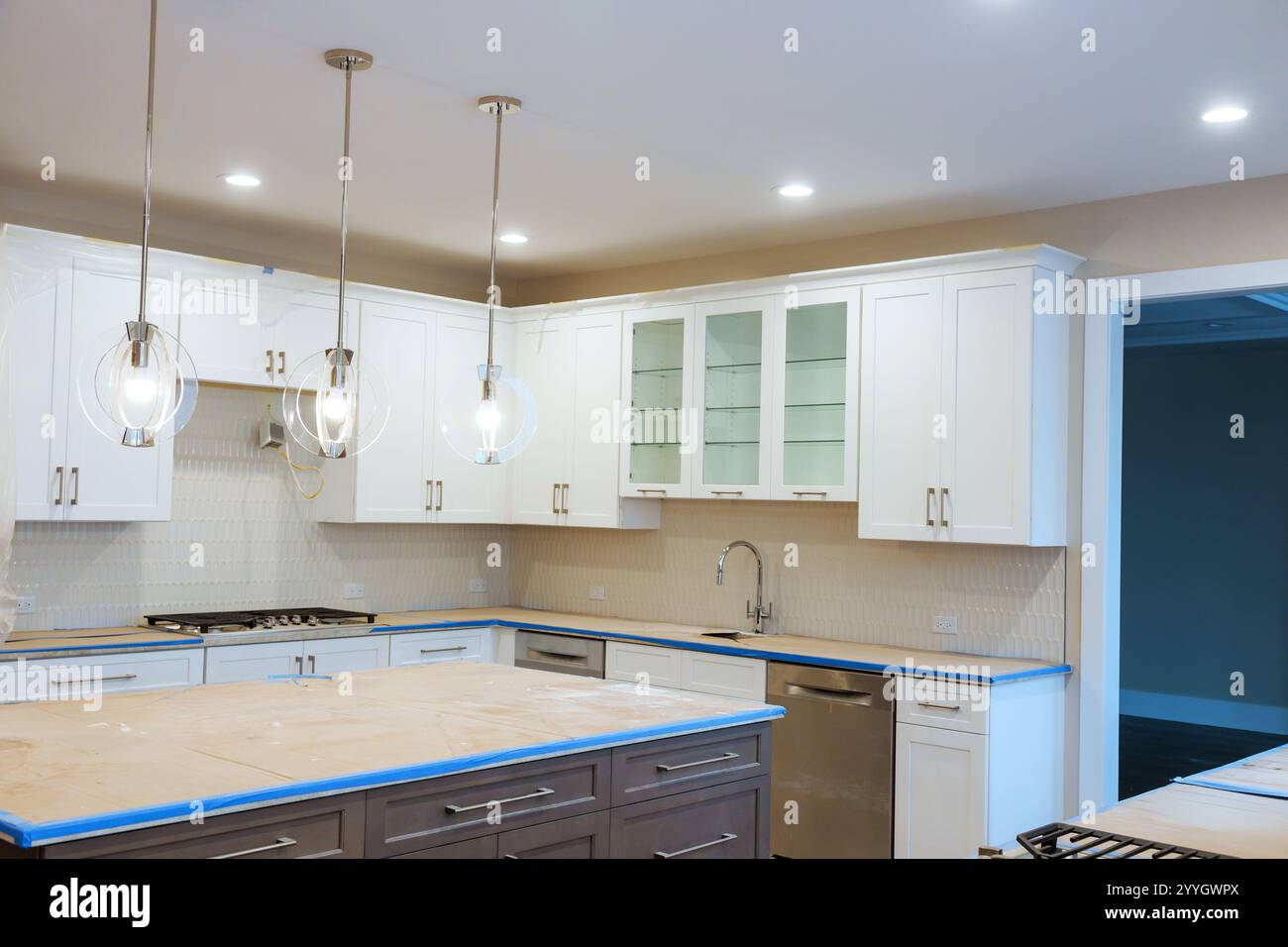 View of Bright kitchen features white cabinets, an island, elegant pendant ...