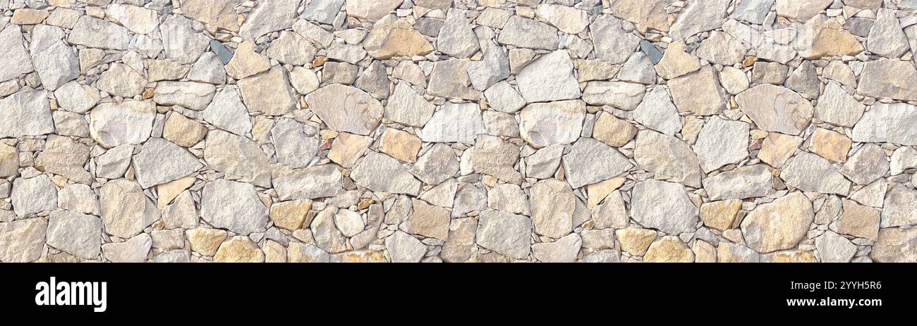 Light brown stone wall in panoramic close-up made of old, roughly hewn, different natural stones Stock Photo