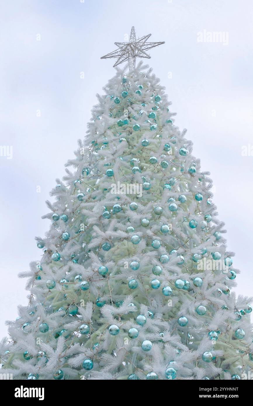 Silver Christmas tree with turquoise New Year's toys. A star on the top of the tree against the sky. Stock Photo