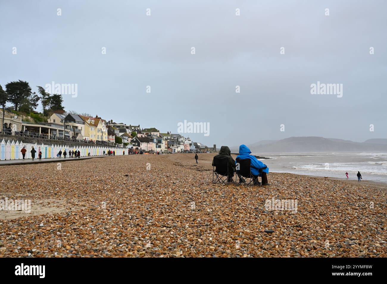 Lyme Regis Dorset UK Winter weekend, couple sitting in the rain on the beach watching the world Stock Photo