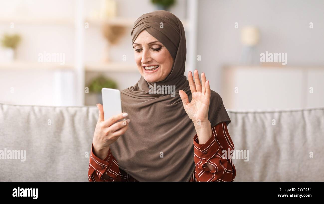 Middle-Aged Muslim Lady Video Calling Via Smartphone Waving Hand Indoor ...