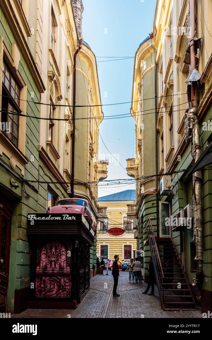 A narrow alleyway with a pink sign that says Freedom Ban. There are several people walking down the street, and a few cars parked along the side. The Stock Photo