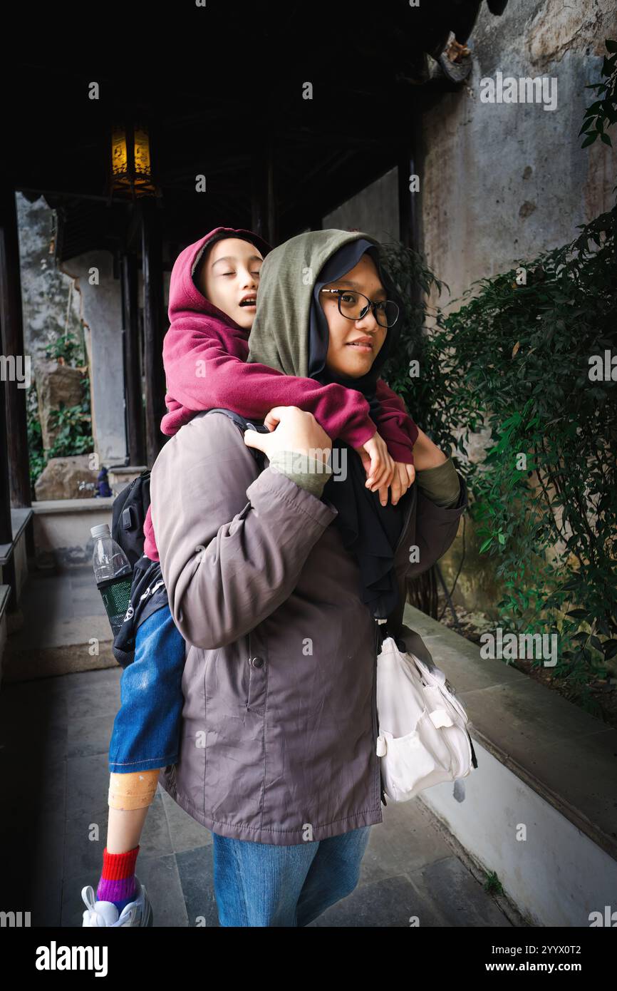 Older sister carrying her tired little girl younger sister on her back. Stock Photo