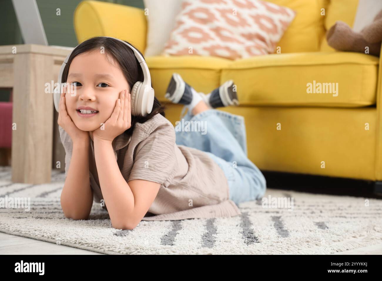 Cute little Asian girl in headphones lying on carpet at home Stock ...