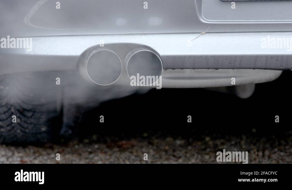 Smoke coming out of dual exhaust pipe of grey, diesel powered car. Shot