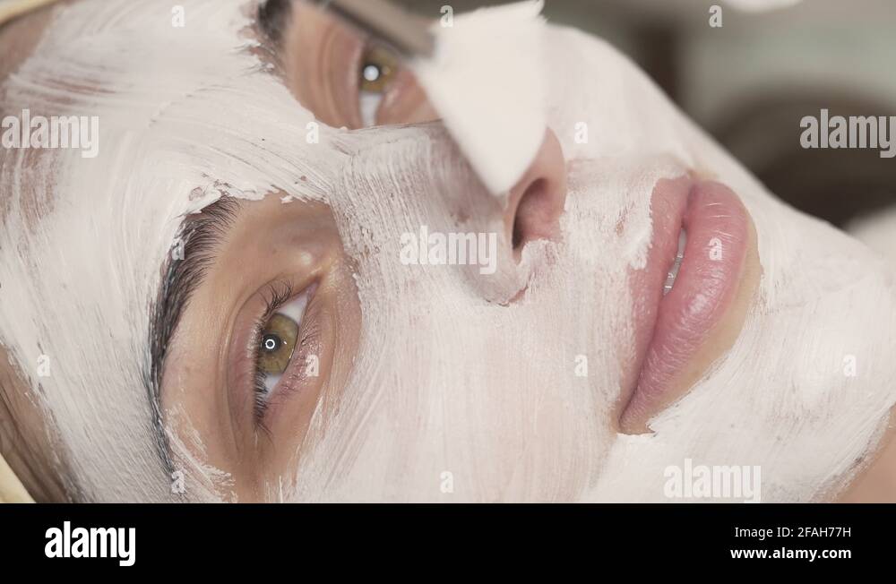 Woman is being applied white mask in beauty salon using special brush