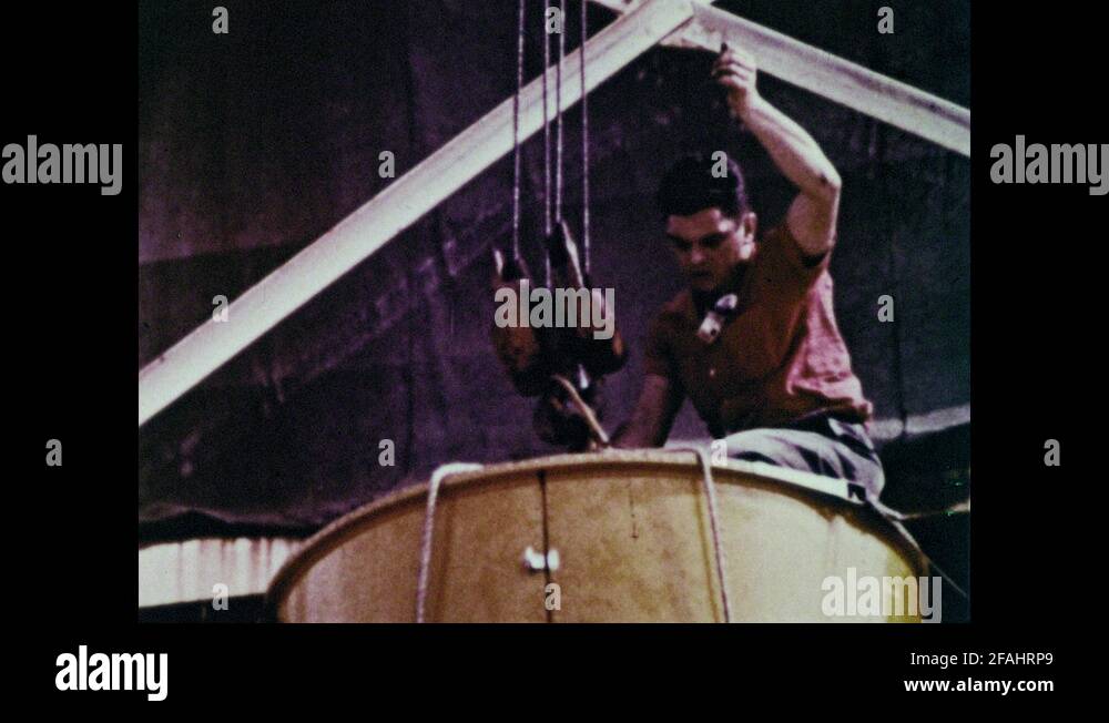 1960s Man gives instructions to crane operator. Crane lifts heavy