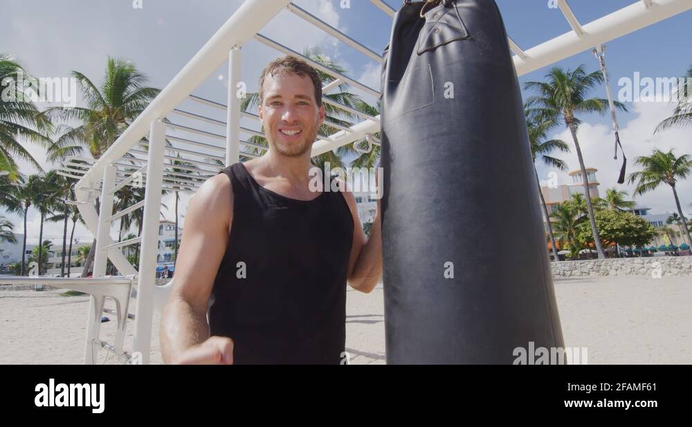 Fitness man flexing arm muscles by boxing punching heavy bag in Outdoor