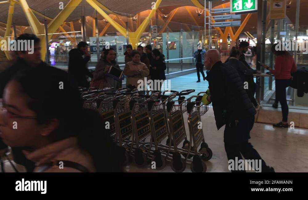 Man pushing baggage dollies in an airport terminal, passengers passing