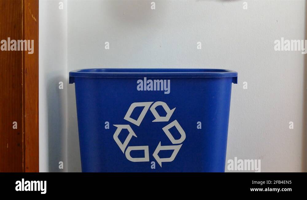 A hand is adding shredded paper in the plastic bag to a recycling bin