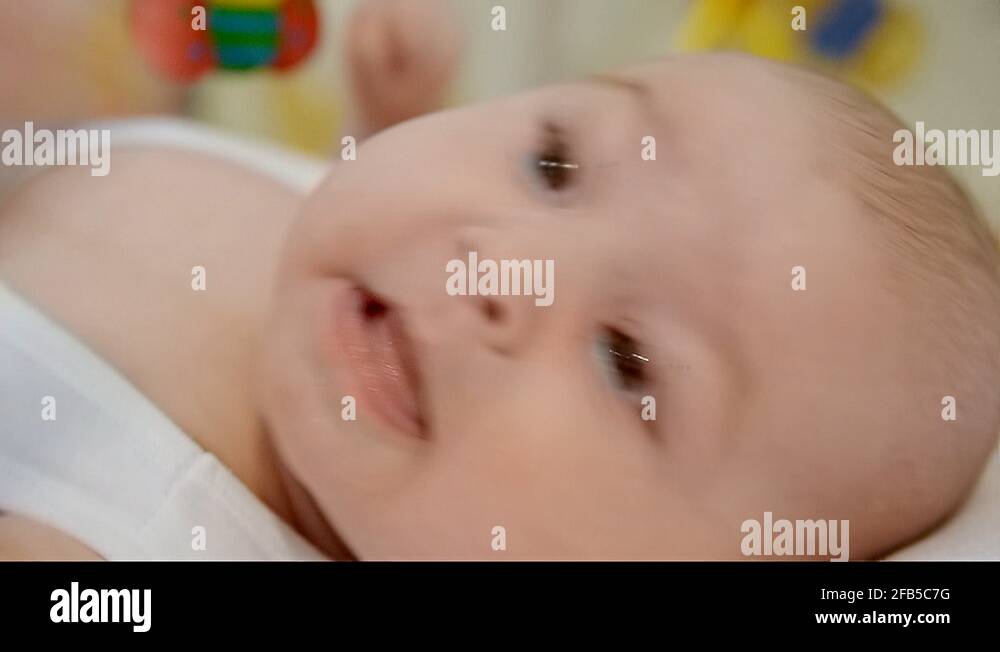 Closeup of the emotional face of a cute baby biting his fist lying on