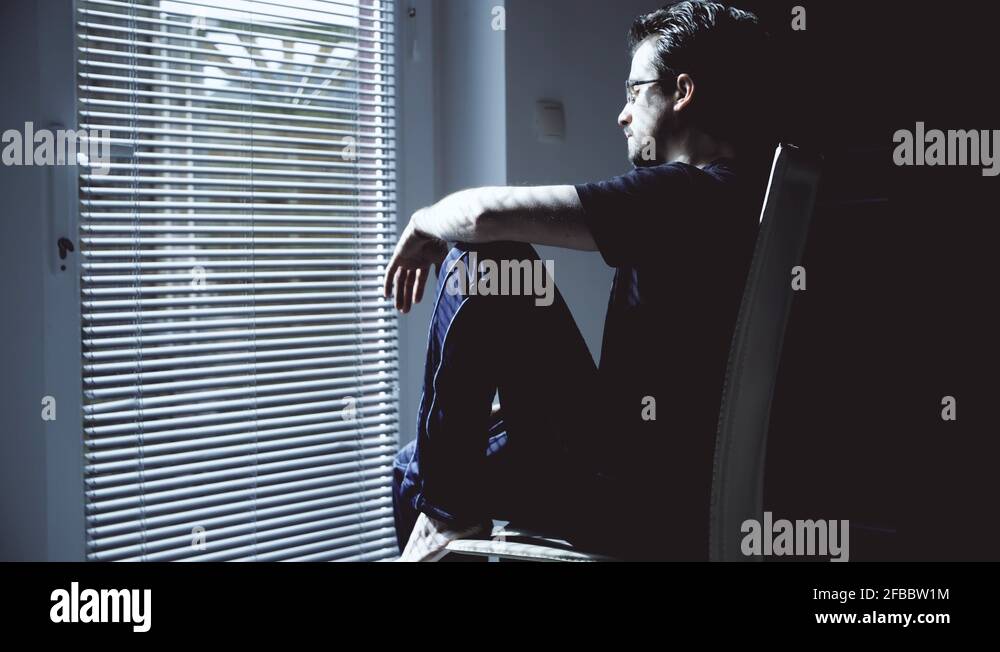 Sad man at the window sitting and put head between legs 4K Stock Video