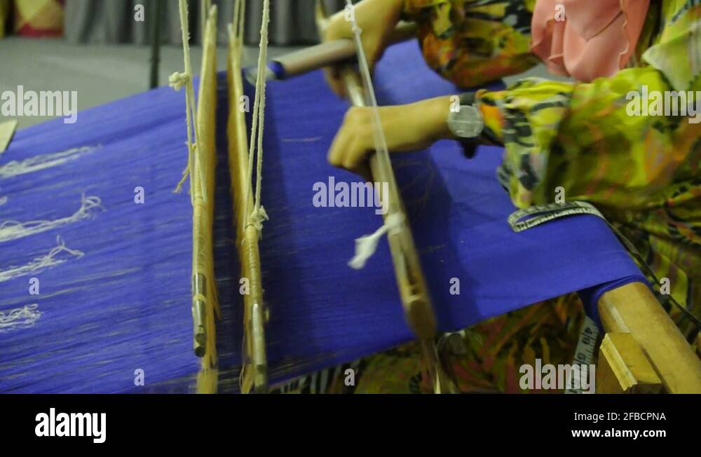 A girl is using traditional weaving machines to weave songket. Songket