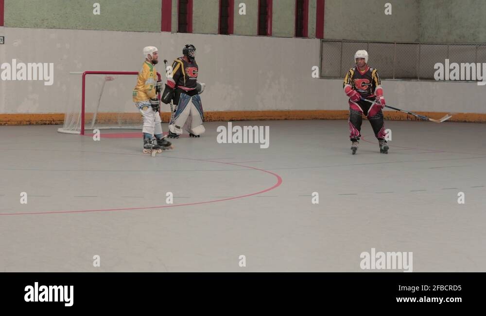 Inline hockey players are positioned in front of goal while goalkeeper