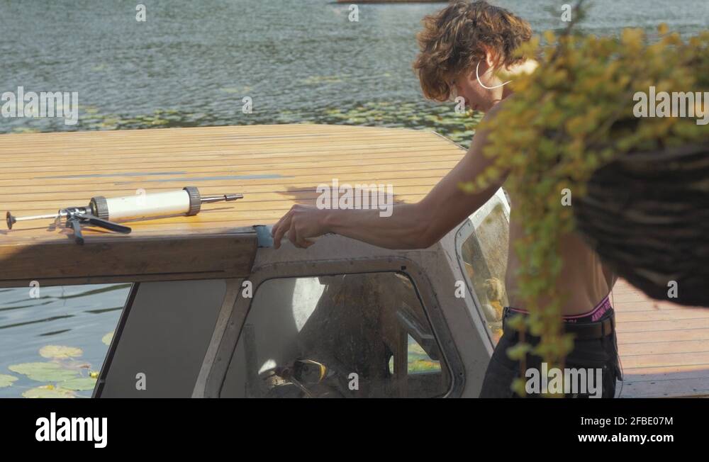 Young working sealing wooden boat cabin roof to prevent leaks using