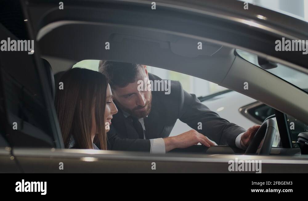 Salesman shows the car features for client. The car is new. Salesman do