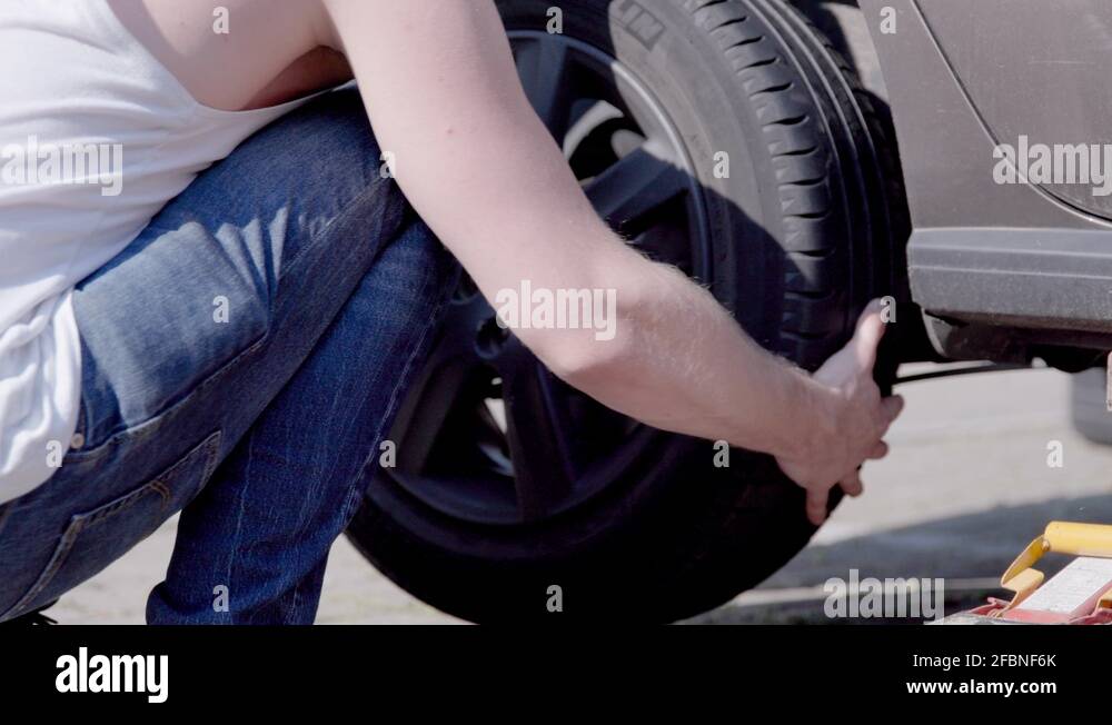 Bearded guy placing wheel on his car's axle during a tire change Stock