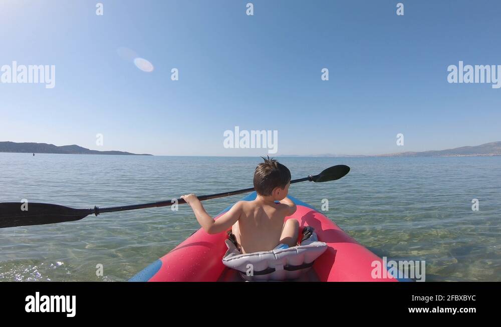 Kid learning kayak. A young boy is paddling towards the horizon on an ...