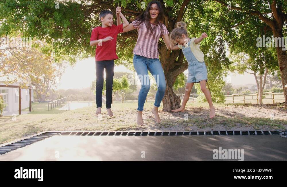 Siblings With Teenage Sister Playing On Outdoor Trampoline In Garden