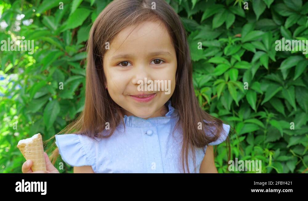 Little cute and funny girl in a blue dress grimaces and eats ice cream