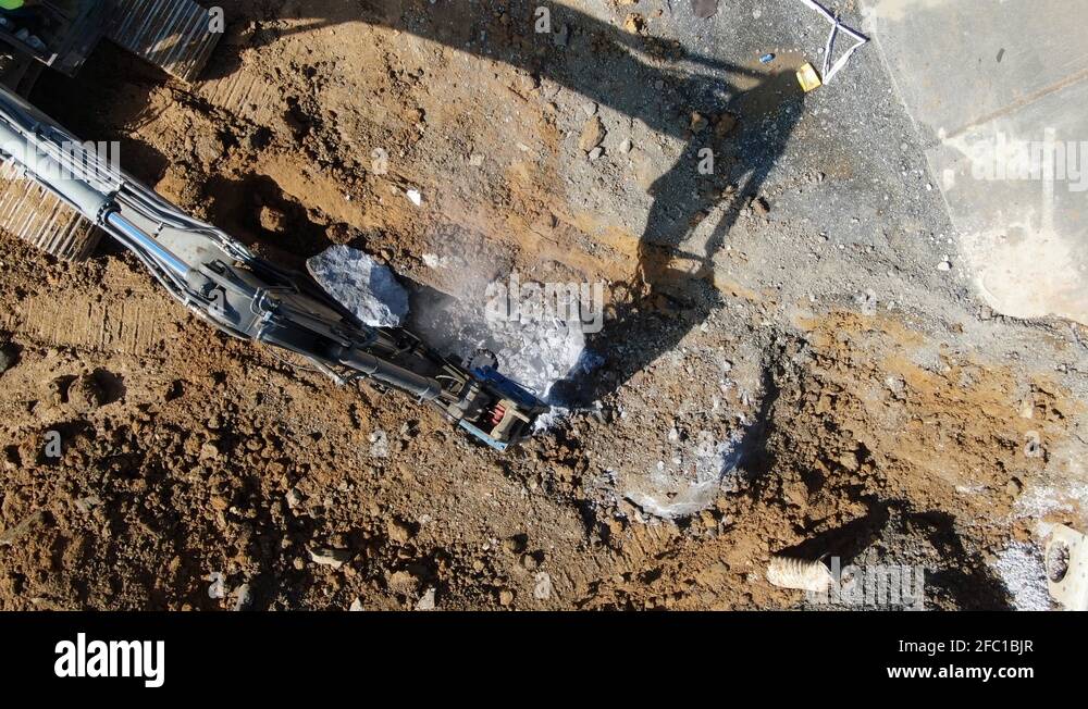 Excavator breaking concrete and limestone with jack hammer attachment