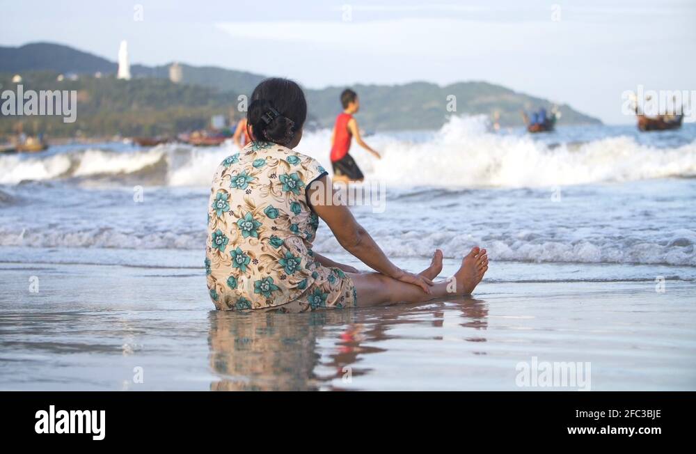 Woman Sat at Beach Shore Line watching her Children Play in Ocean. Mother Stock Video Footage