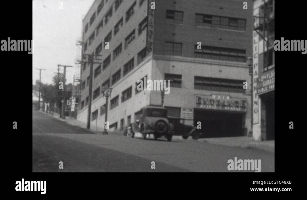 1920s: Cars drive down street. Tall buildings. Man walks down street ...