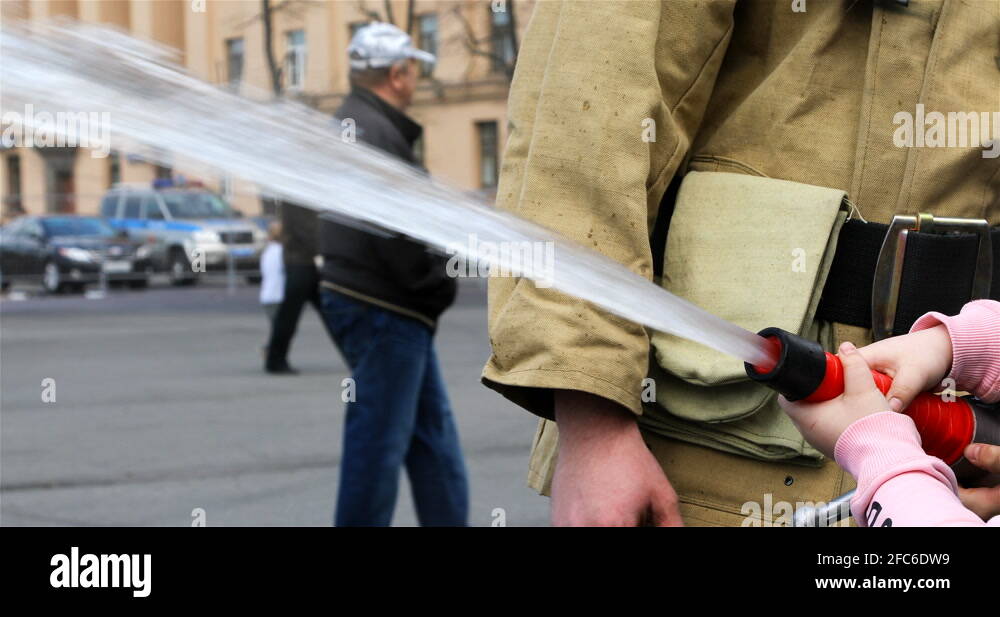 fireman in a special form teaches children to hold the fire hose for