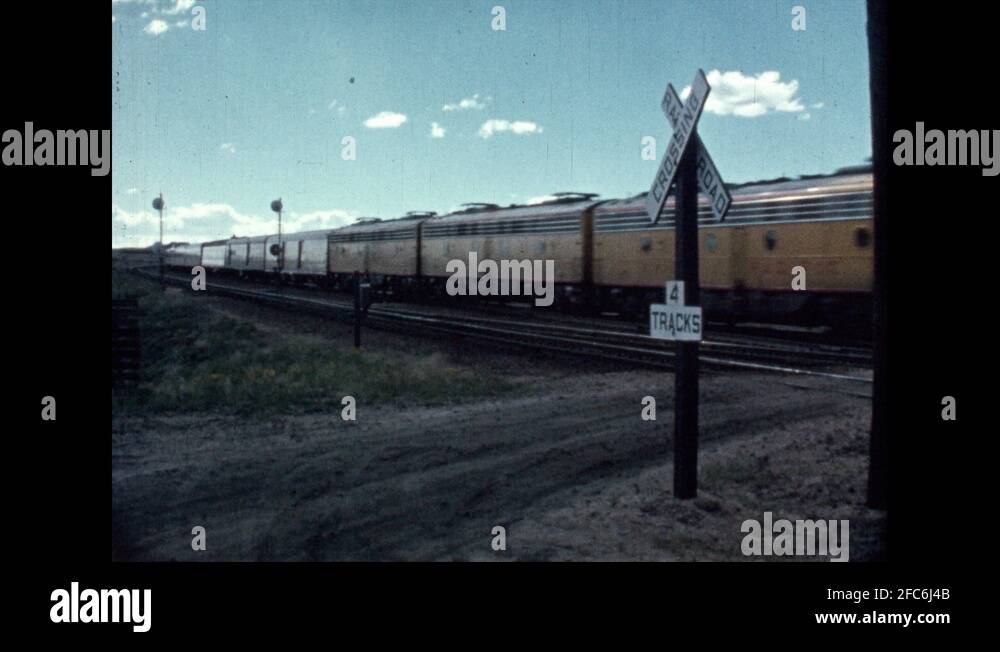 1950s Train goes over road at railroad crossing. Railroad Crossing