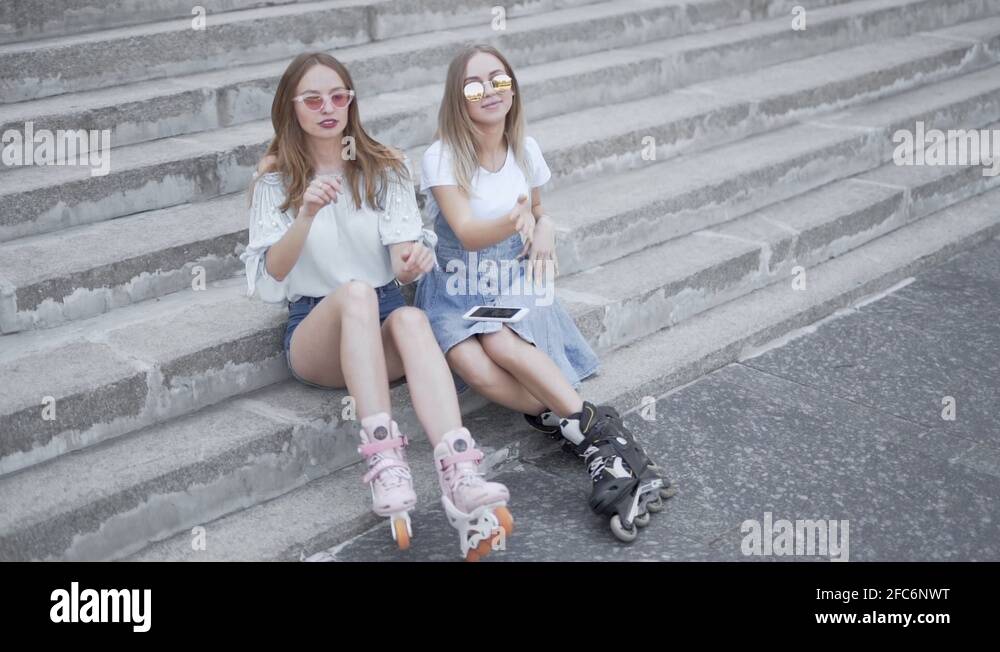 Two young sporty girls sitting on steps dancing to music with roller skates Stock Video Footage