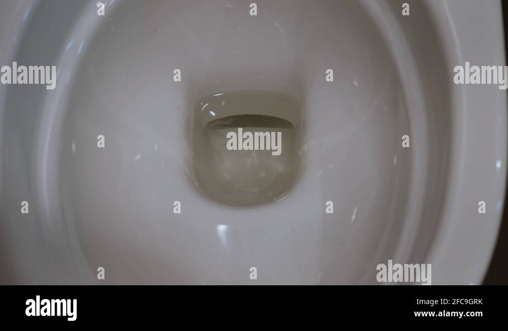 A stream of water flows down into the white toilet bowl. The whirlpool ...