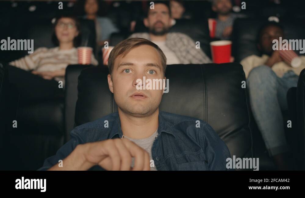 Shocked student watching film in cinema with open mouth eating popcorn
