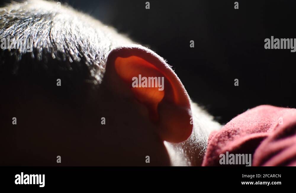 Anonymous young boy in dark room backlit red ear. Conceptual anxiety