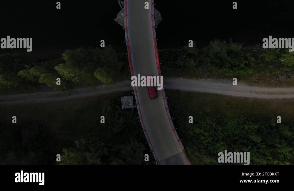 Topdown drone footage showing a red car driving over a narrow bridge that Stock Video Footage