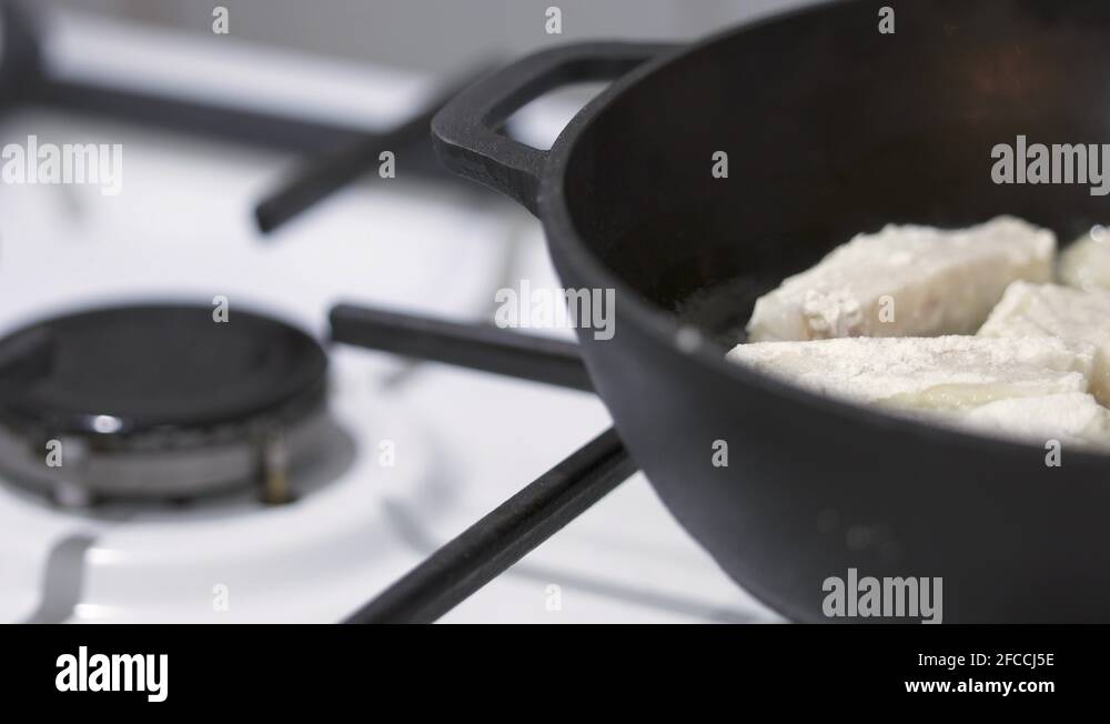 Making pan fried cod fish fillet in cast iron frying pan with cooking