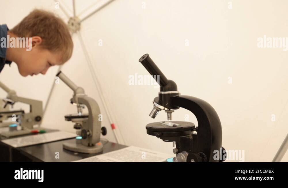 White little 9 years old kid looking through microscope. Blurry face