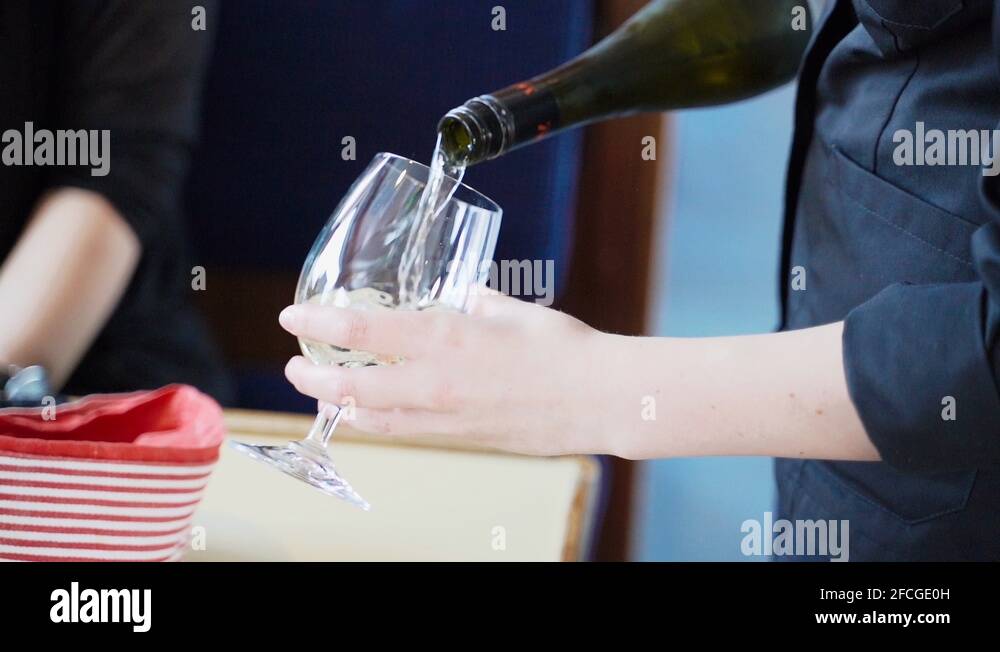 Waitress pouring white wine from bottle into glass to serve customer