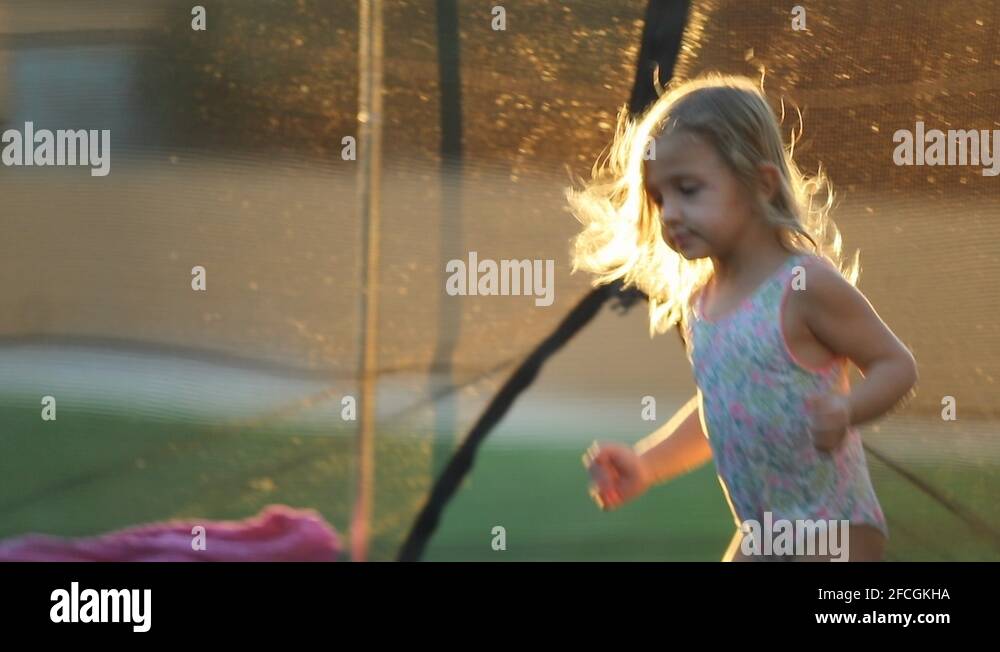 Happy Little girl bouncing up and down on trampoline outside feeling