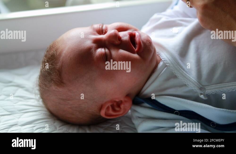 Upset baby crying having a tantrum while mother puts clothes on infant