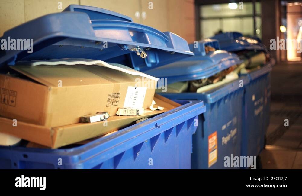 Overflowing trash container waste bin with old paper and boxes in night